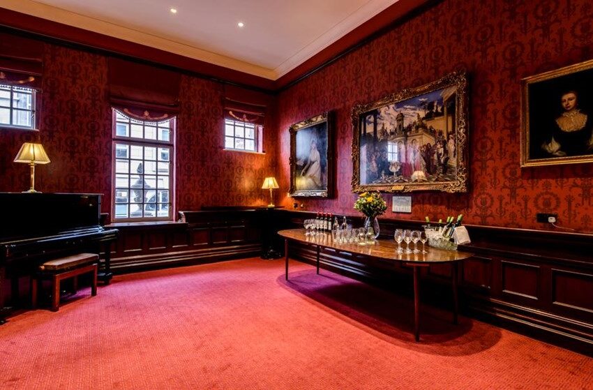 The Ellis Room at the London Coliseum - a plush room with red walls and carpet and piano set up for drinks reception