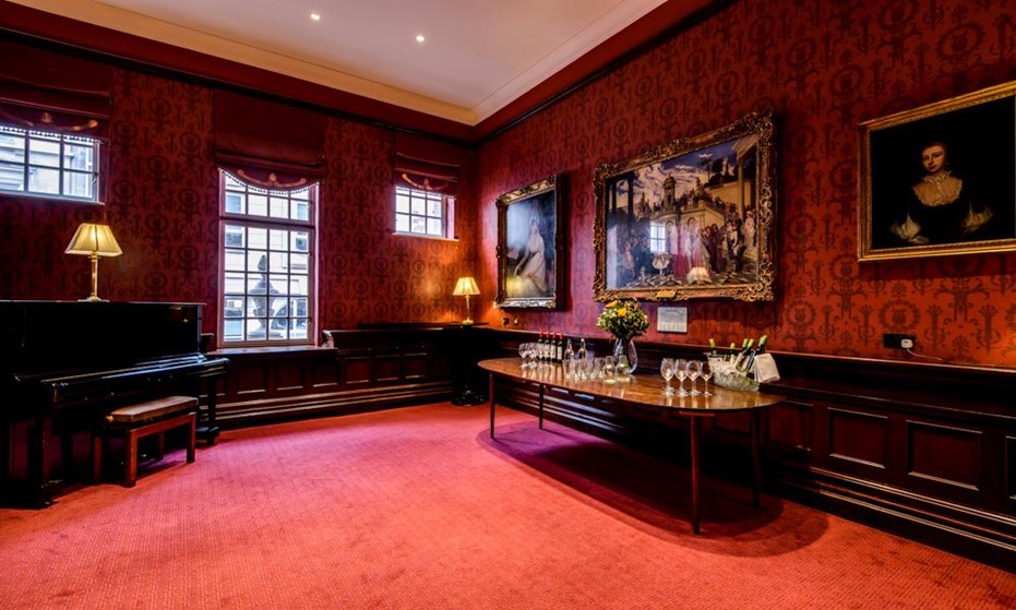 Plush room with red walls and carpet and piano set up for drinks reception
