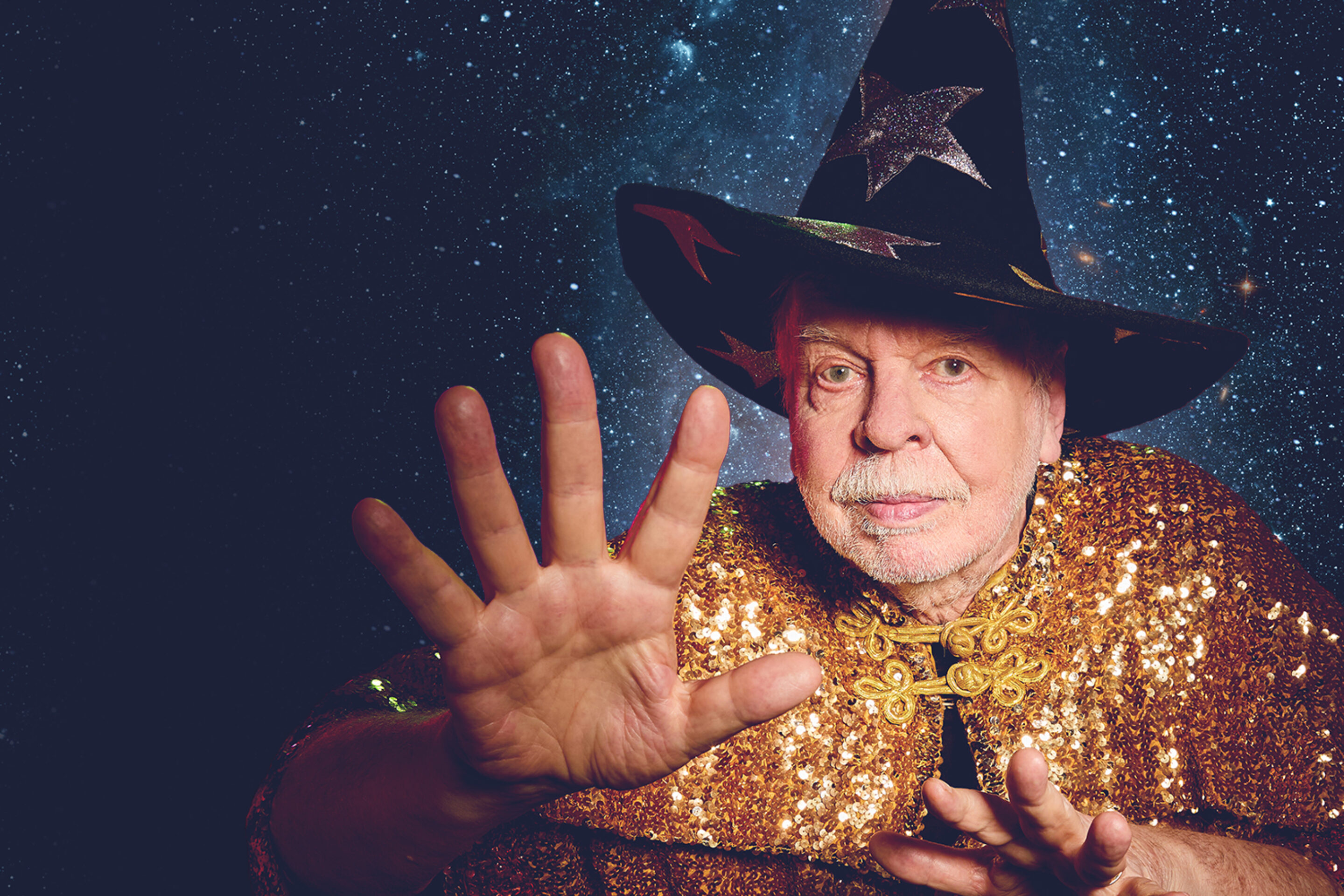 Image of Rick Wakeman in a wizard hat and robe with his hand reaching forward