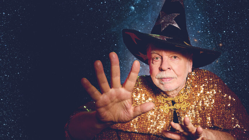 Image of Rick Wakeman in a wizard hat and robe with his hand reaching forward