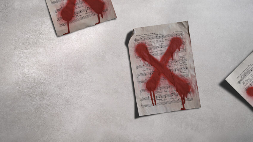 Three sheets of music lie on a grey surface, each marked with a large, red, painted X that appears to be dripping, suggesting rejection or censorship.