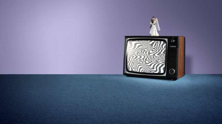 A vintage TV with static, wavy black-and-white lines on the screen sits on blue carpet. On top of the TV is a bride and groom wedding cake topper, set against a purple background.