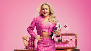 Image of Amber Davies as Elle Woods in Legally Blonde stood in front of pink luggage and a small dog.